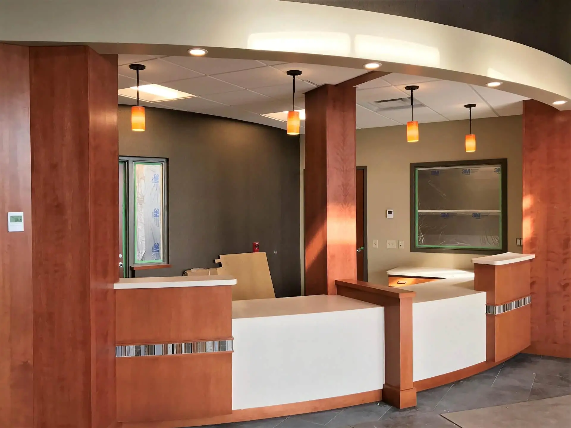 Modern reception area with wood-paneled desks, white countertops, pendant lights, and dark tiled flooring