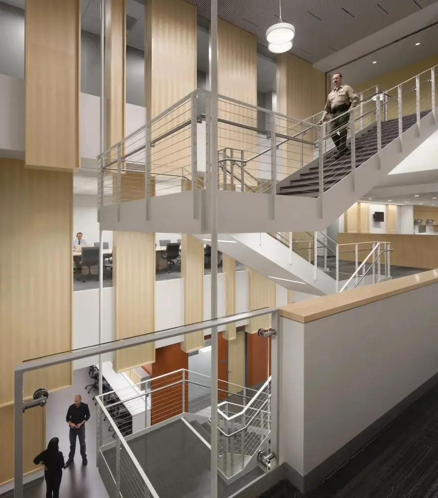 Multi-level office interior with open staircases, metal railings, wood panels, desks, and several people
