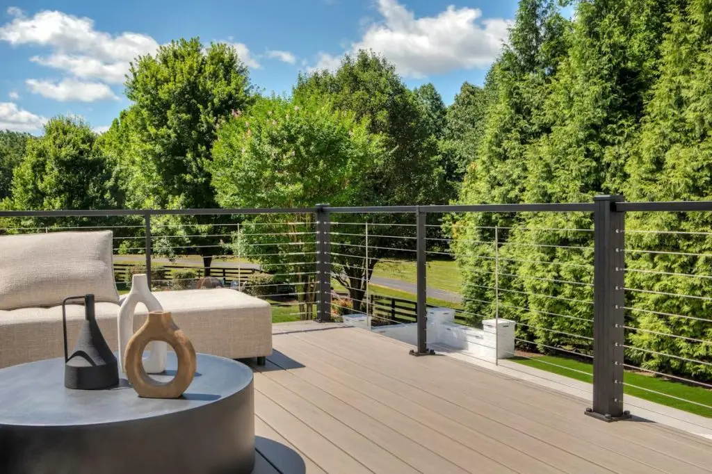 Contemporary deck with lounge seating, decorative vases, and cable railing overlooking a tree-filled yard