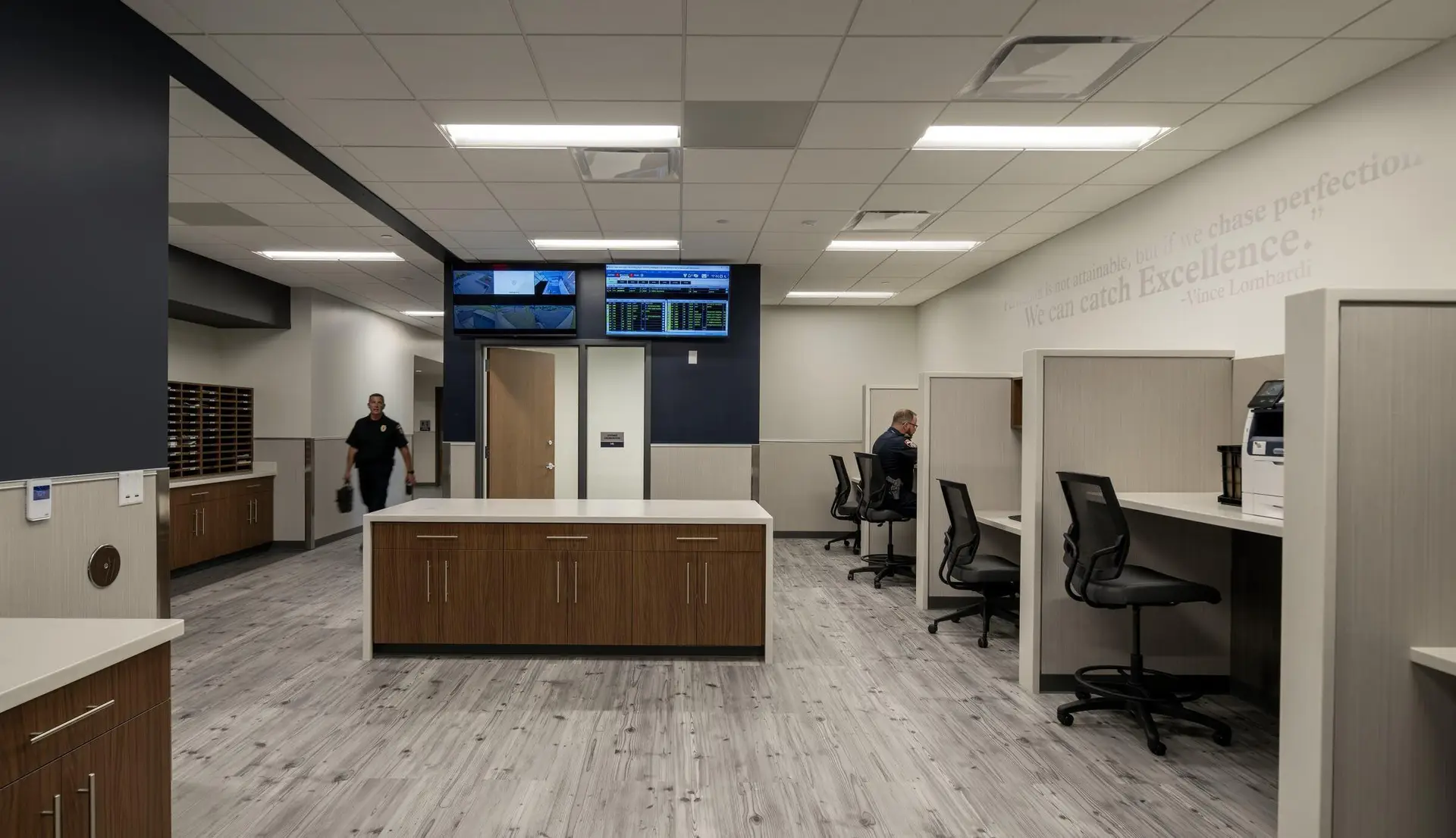 Modern office interior with workstations, computer monitors, cabinetry, and two people