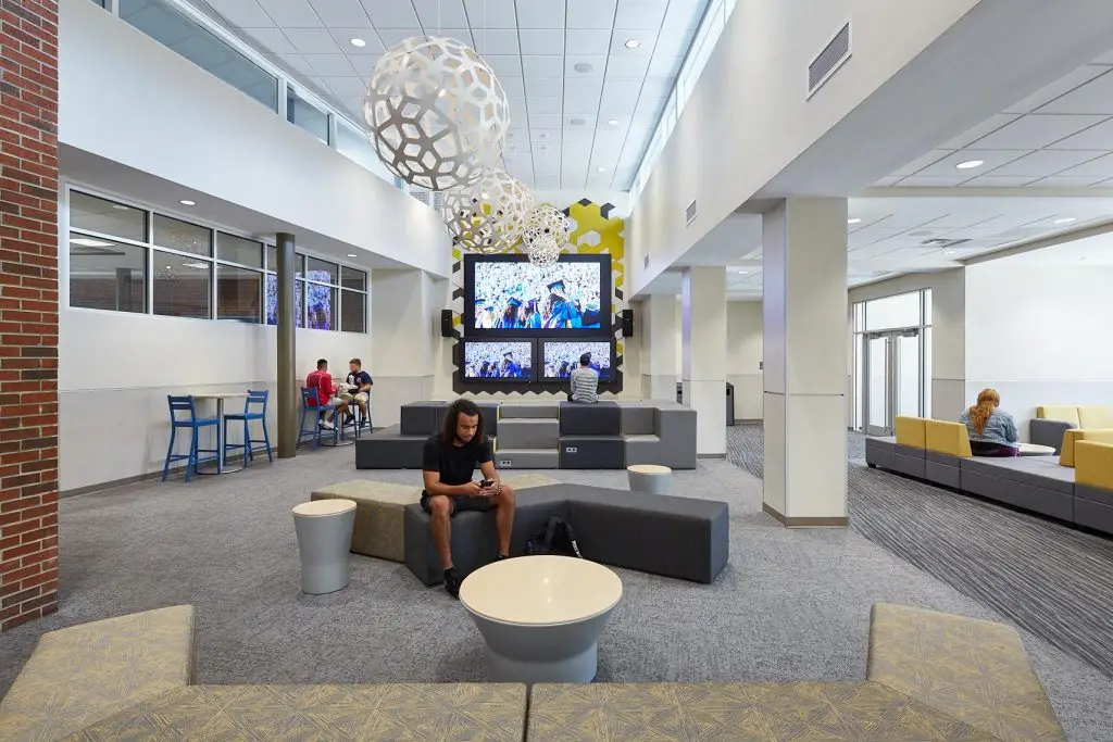 Modern indoor lounge with seating, tables, decorative hanging spheres, and multiple media screens