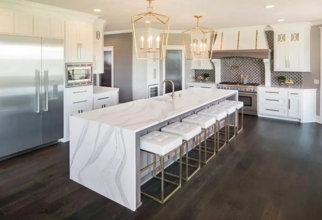 Bright modern kitchen with white cabinets, a large veined island, pendant lights, dark floors, and bar stools.